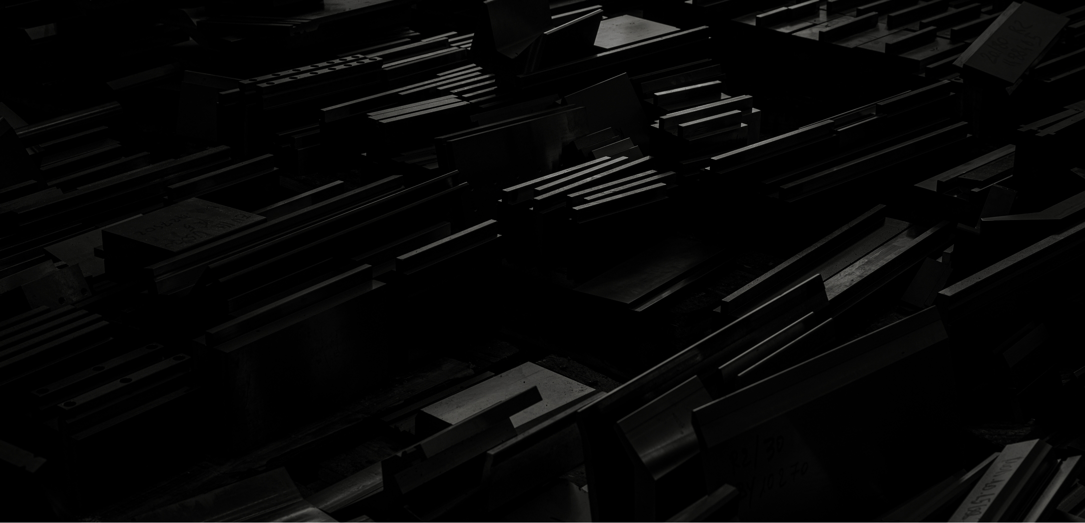 Dark-toned warehouse background with neatly stacked metal tooling components, used as a design element for company statistics.