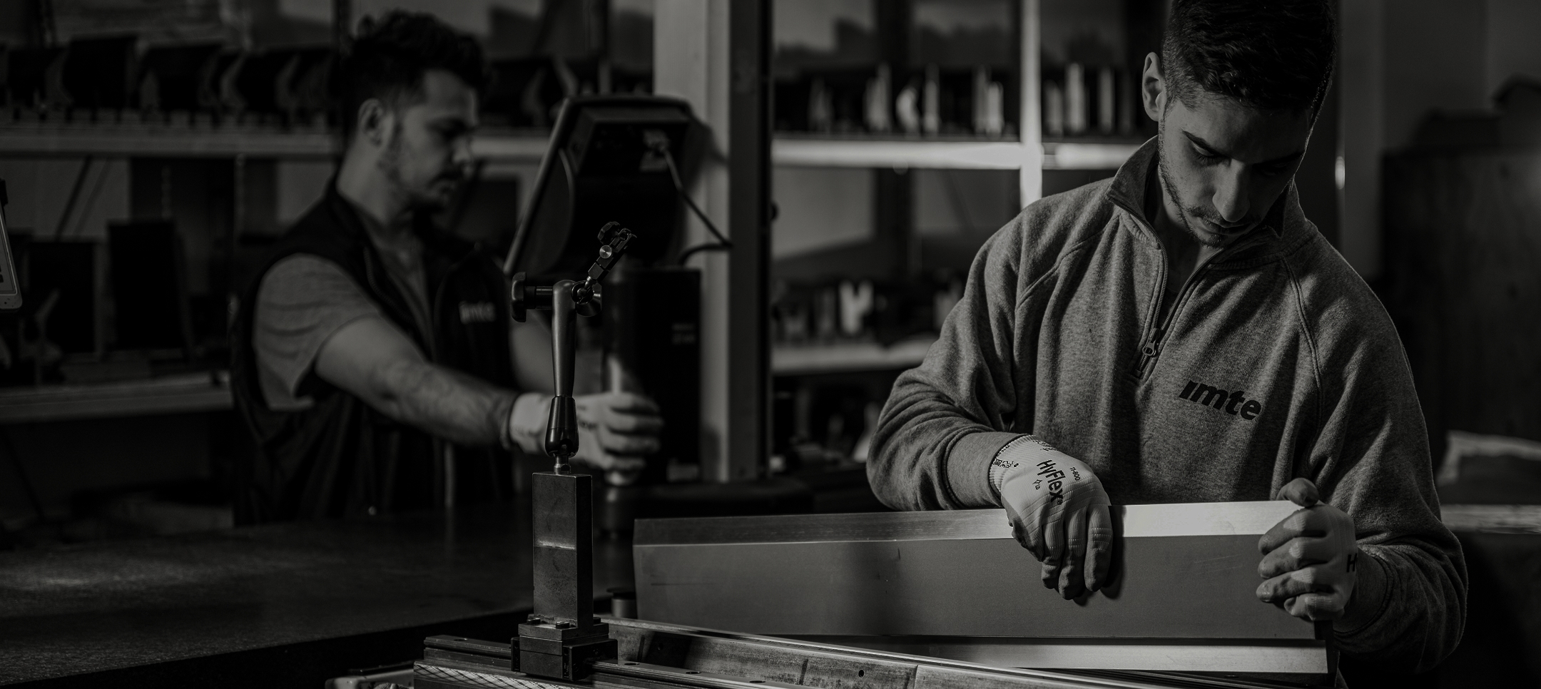 Two IMTE technicians in a workshop inspecting and measuring a press brake tool with precision equipment, emphasizing craftsmanship and engineering expertise.